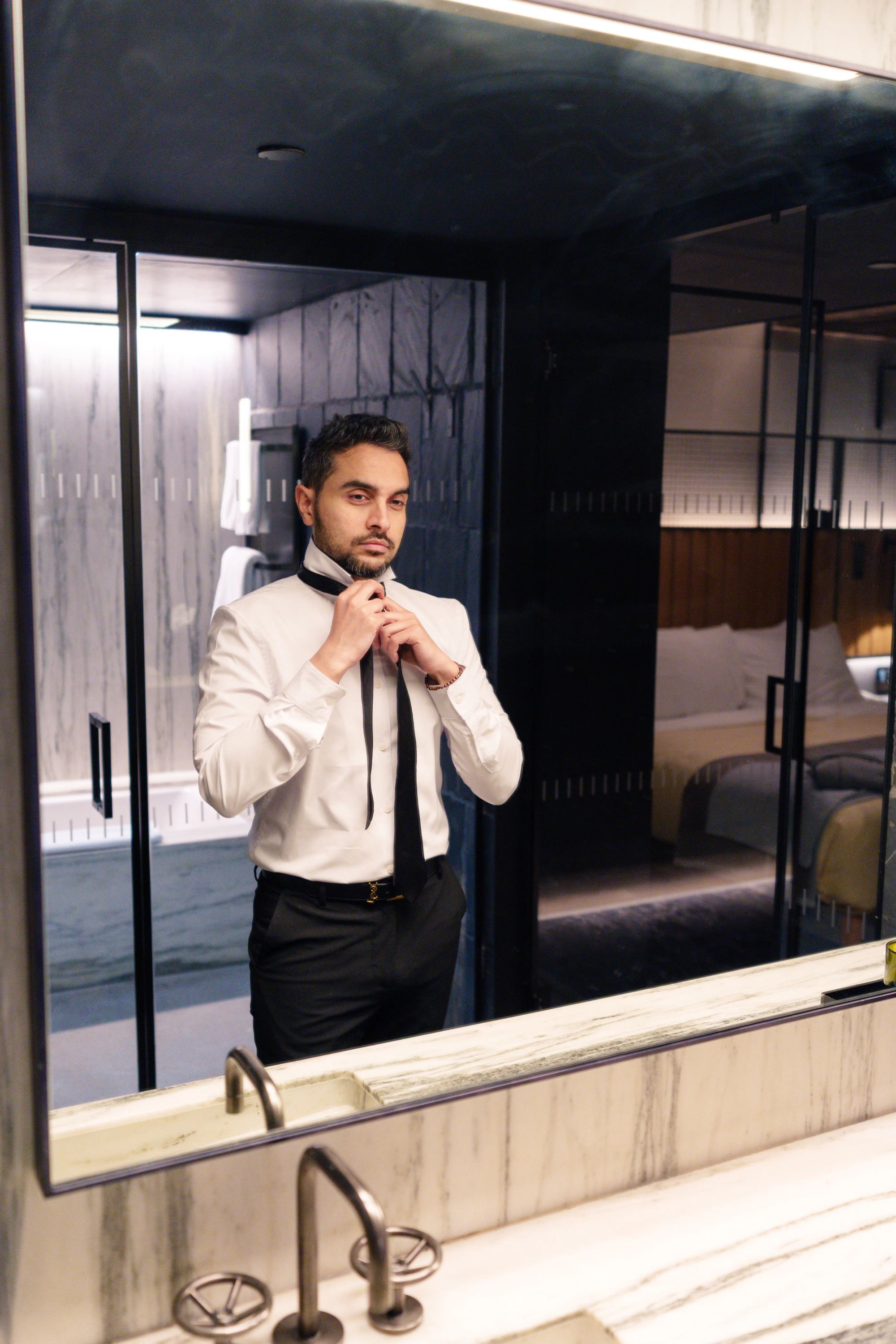 A guest dressing at the mirror in a dark stone suite bathroom