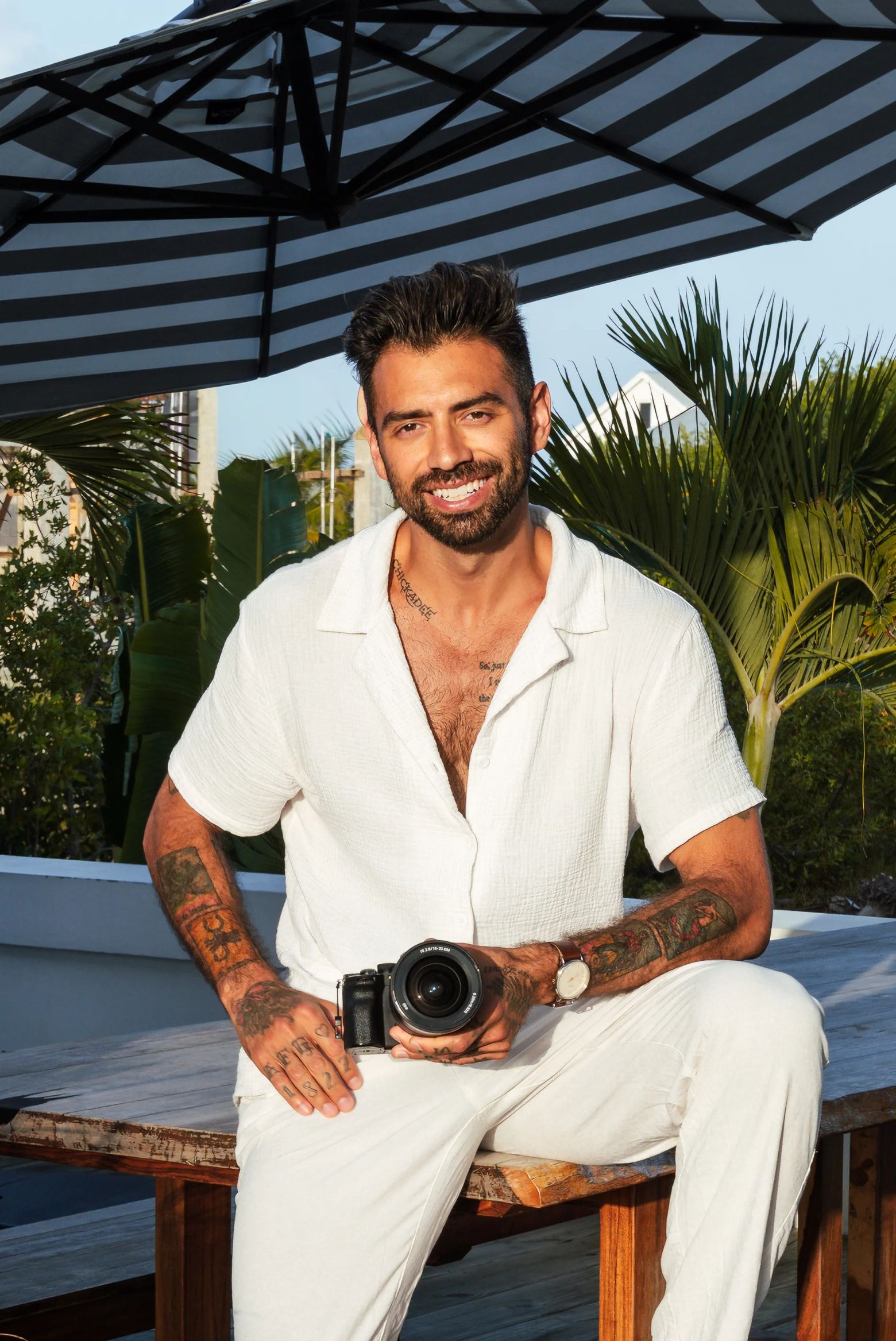 Vincent Del Toral seated with a camera, under a parasol on a terrace